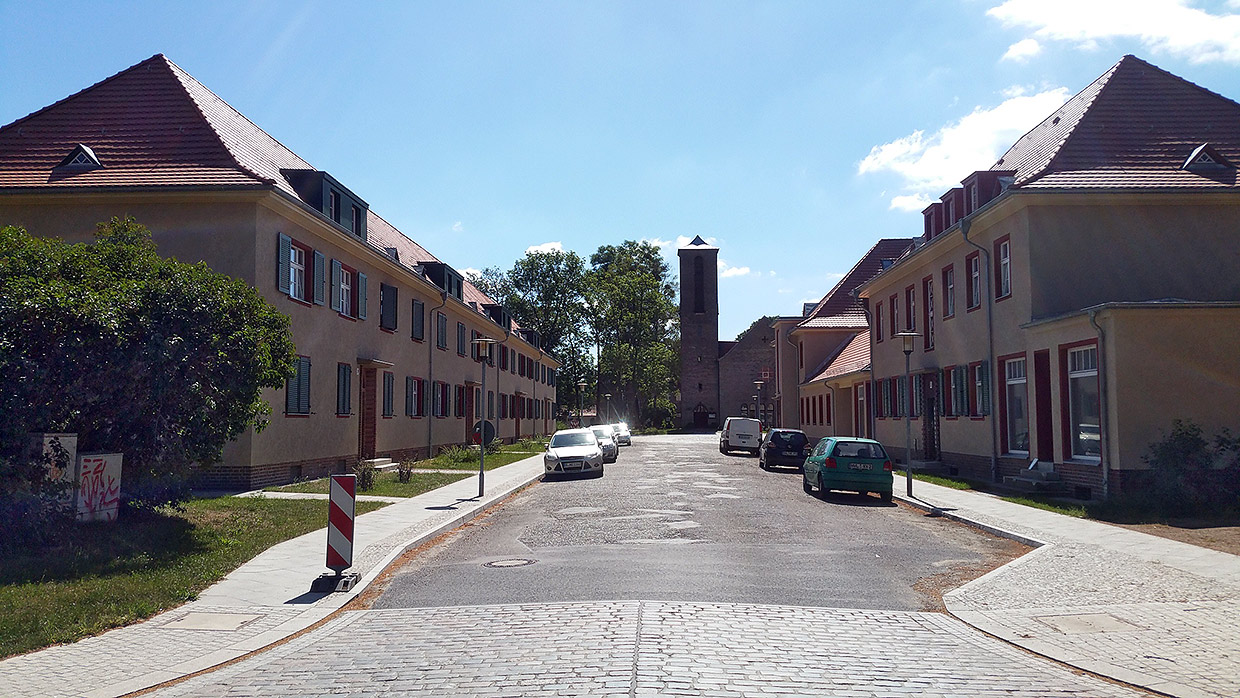 Strassenansicht am Karl-Liebknecht-Platz mit Siedlungskirche Elstal . Sanierung Eisenbahnersiedlung, Elstal/ Wustermark